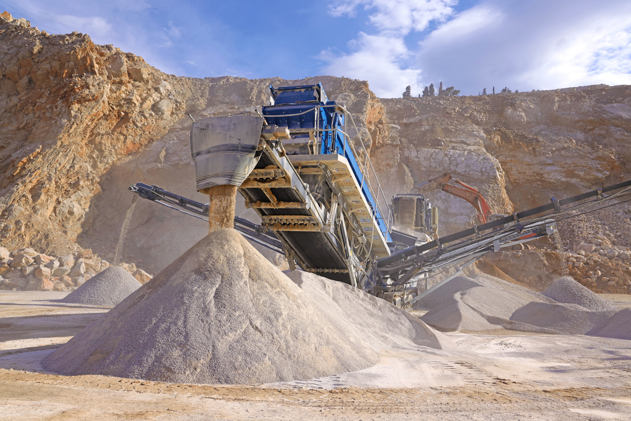 Stone crushing machine at open pit mining and processing plant for crushed stone. Piles of gravel stone and conveyor belts on the side of the road. Concepts of industry and building materials, sand and gravel