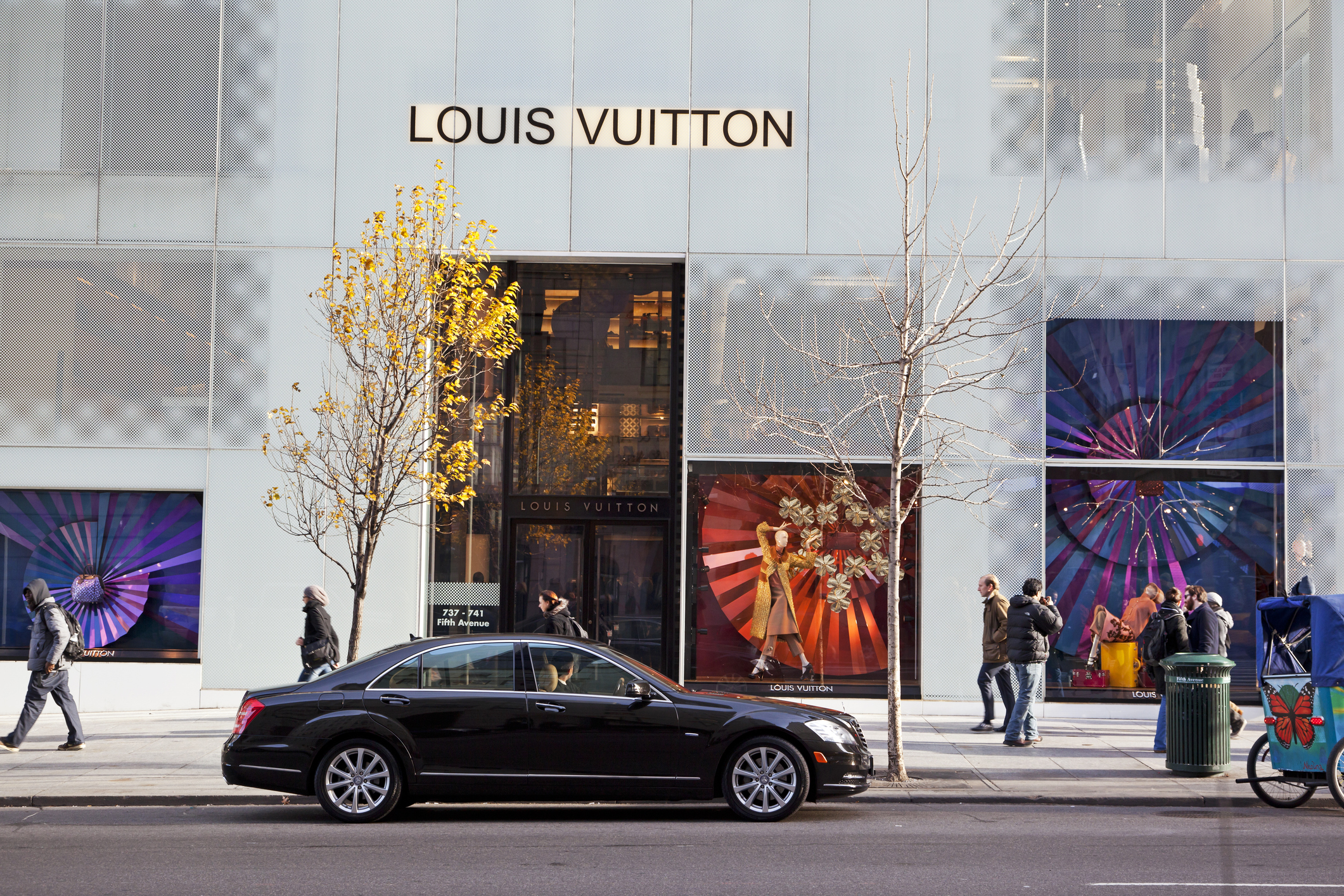 "New York City, USA - December 6, 2012: People walking on the sidewalk in front of the Louis Vuitton store at Fifth avenue. A luxury car with driver is  waiting in front of the store."
