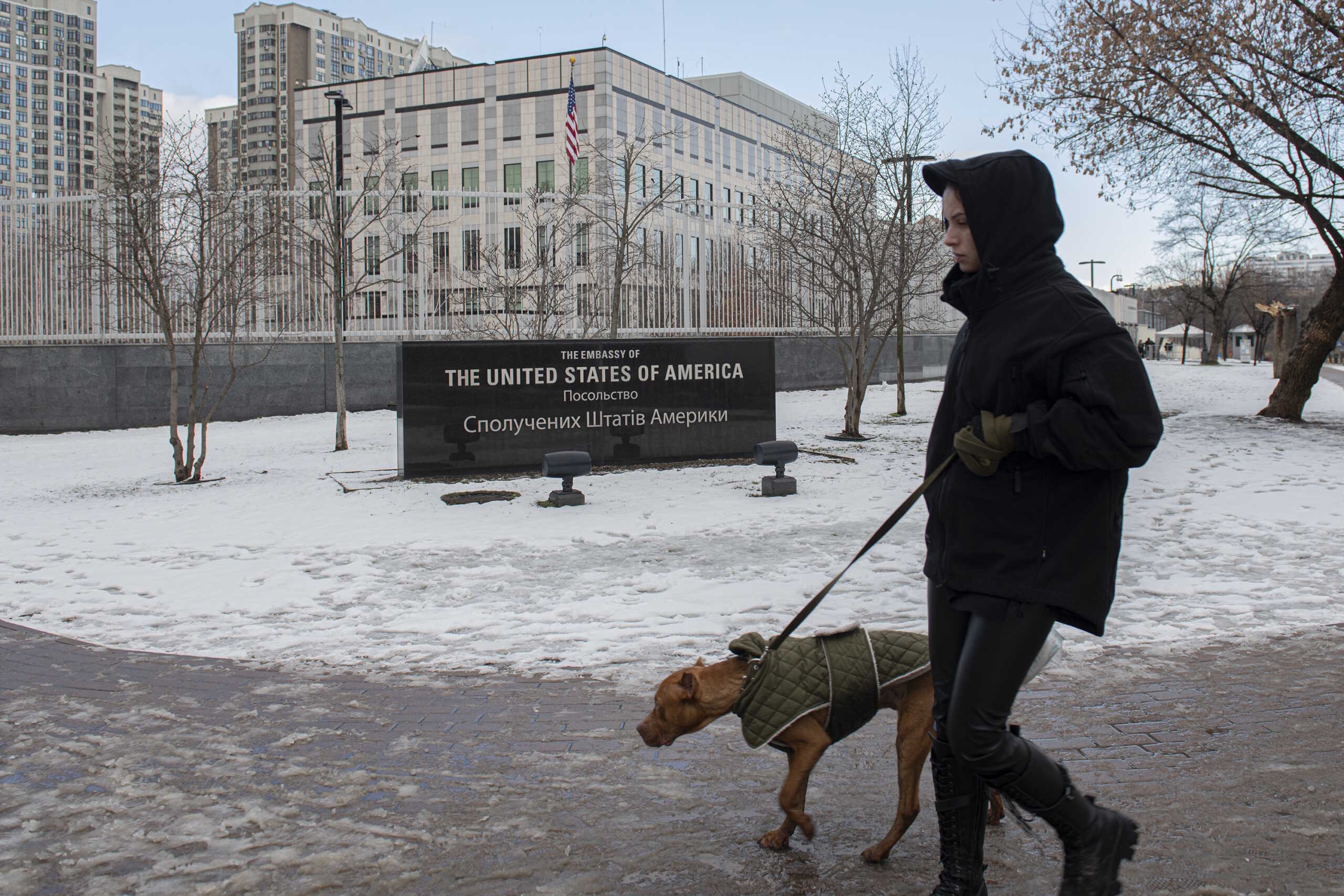 A man walks with his dog in front of the U.S. Embassy in Kyiv, Ukraine, Saturday, Feb. 12, 2022. U.S. officials told The Associated Press that the State Department plans to announce Saturday that virtually all American staff at the Kyiv embassy will be required to leave. The State Department would not comment. The department had earlier ordered families of U.S. embassy staffers in Kyiv to leave. But it had left it to the discretion of nonessential personnel if they wanted to depart. (AP Photo