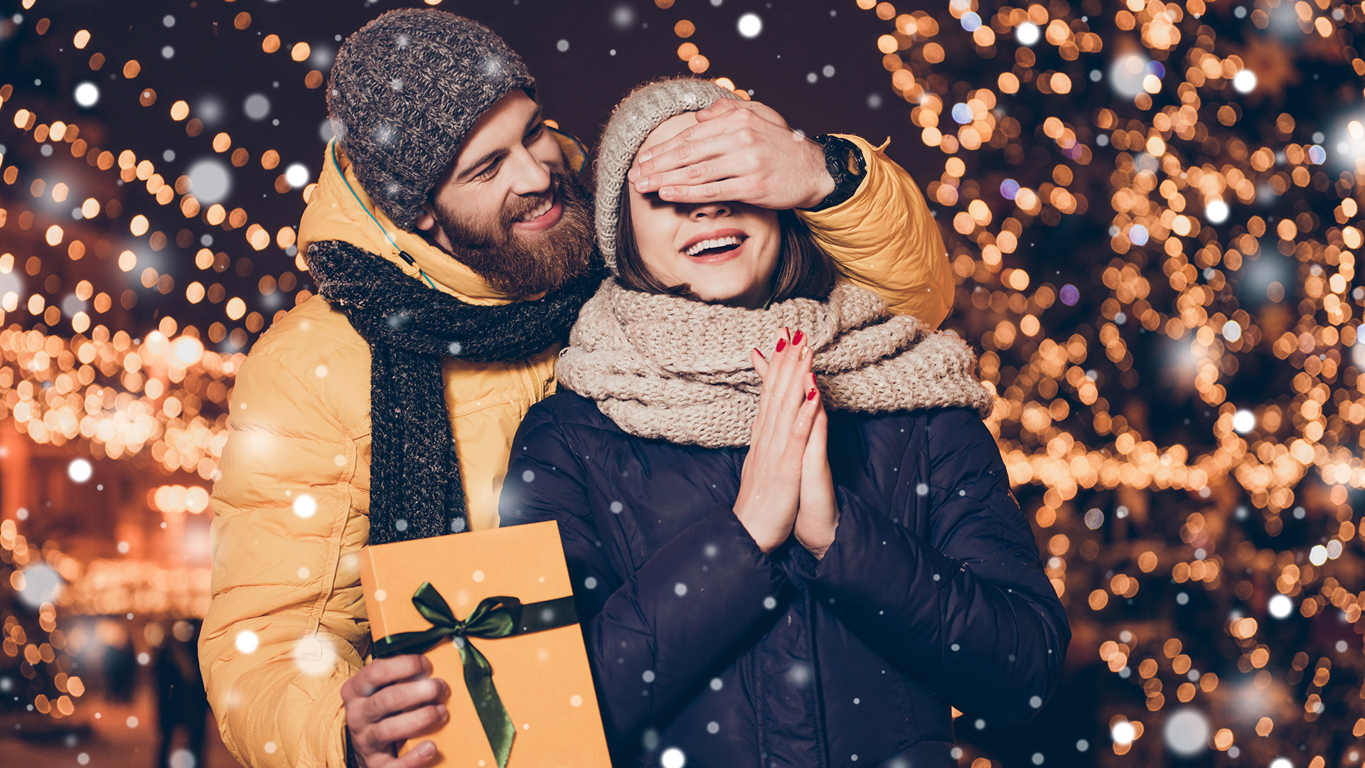 Have something for you dear! Smiling cute brunette is waiting for surprise from her lover, who closed her eyes with hand. Christmas eve outdoors, many lights around