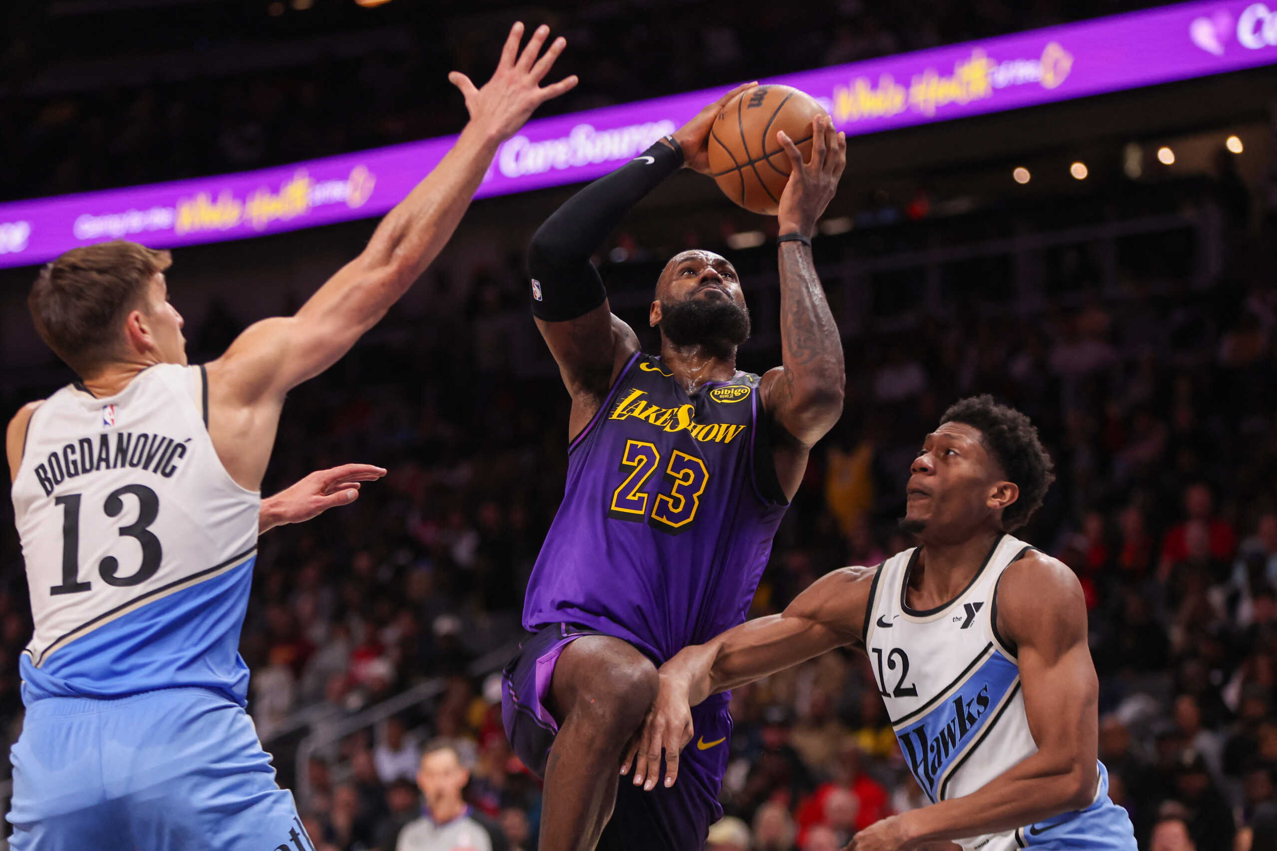 Dec 6, 2024; Atlanta, Georgia, USA; Los Angeles Lakers forward LeBron James (23) shoots past Atlanta Hawks guard Bogdan Bogdanovic (13) and forward De'Andre Hunter (12) in the second quarter at State Farm Arena. Mandatory Credit: Brett Davis-Imagn Images