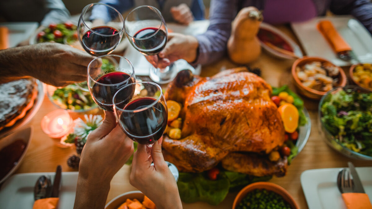 Group of unrecognizable people toasting with wine during Thanksgiving dinner at dining table.