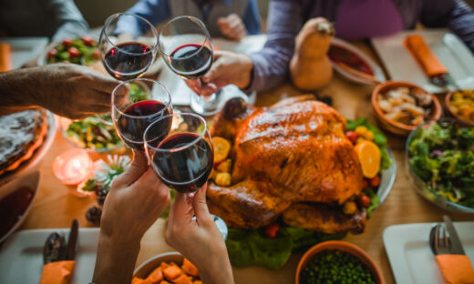 Group of unrecognizable people toasting with wine during Thanksgiving dinner at dining table.