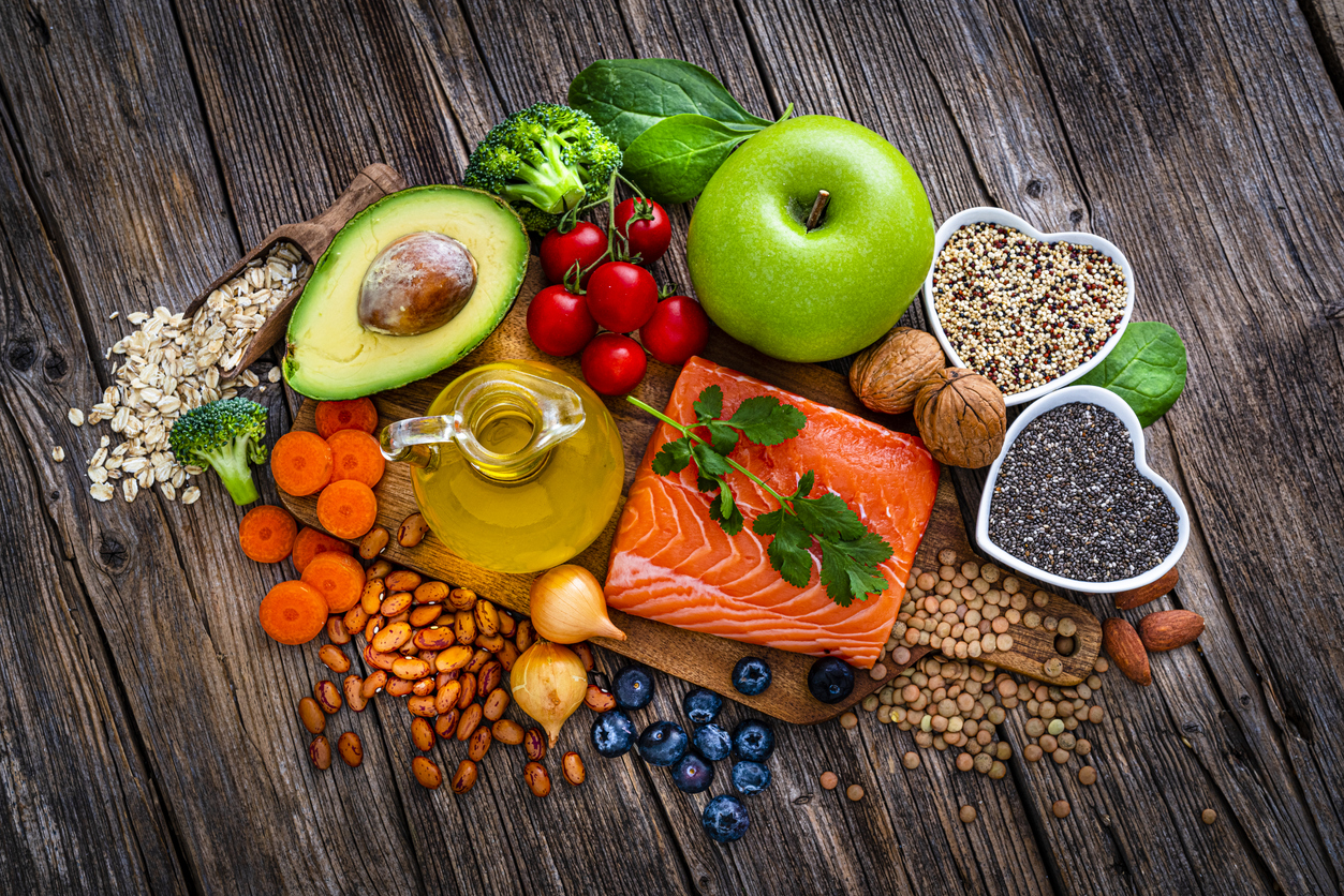 Overhead view of a group of food for heart care and lower cholesterol shot on rustic wooden table. The composition includes salmon, olive oil, chia seeds, quinoa, broccoli, avocado, green apple, oatmeal, spinach, brown lwntil, pinto bean, onion, almonds, walnut, carrot blueberries among others. High resolution 42Mp studio digital capture taken with SONY A7rII and Zeiss Batis 40mm F2.0 CF lens
