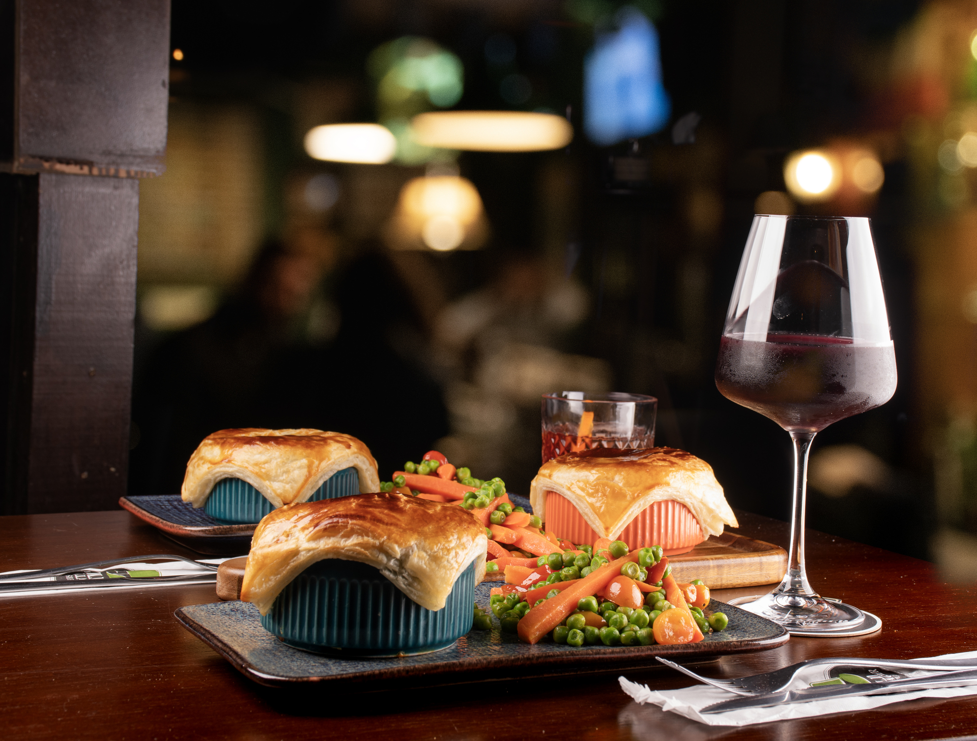 three Irish savory pies baked with puff pastry served with vegetables dinner paired with red wine and drink in a restaurant