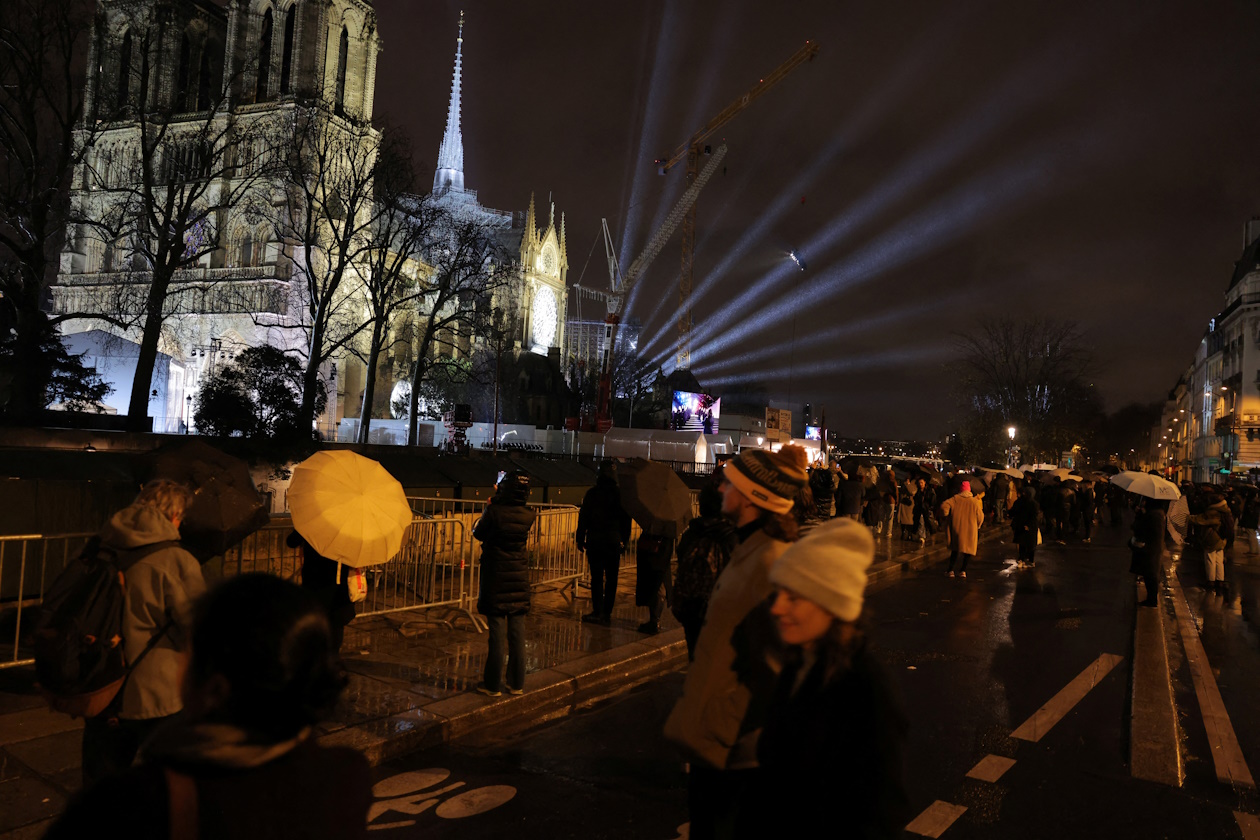 People protect themselves from the rain under umbrellas as they walk in a security perimeter near the Notre-Dame de Paris Cathedral, five-and-a-half years after a fire ravaged the Gothic masterpiece, to listen its reopening service ceremony as part ceremonies to mark the Cathedral's reopening after its restoration, in Paris, France, December 7, 2024.  REUTERS