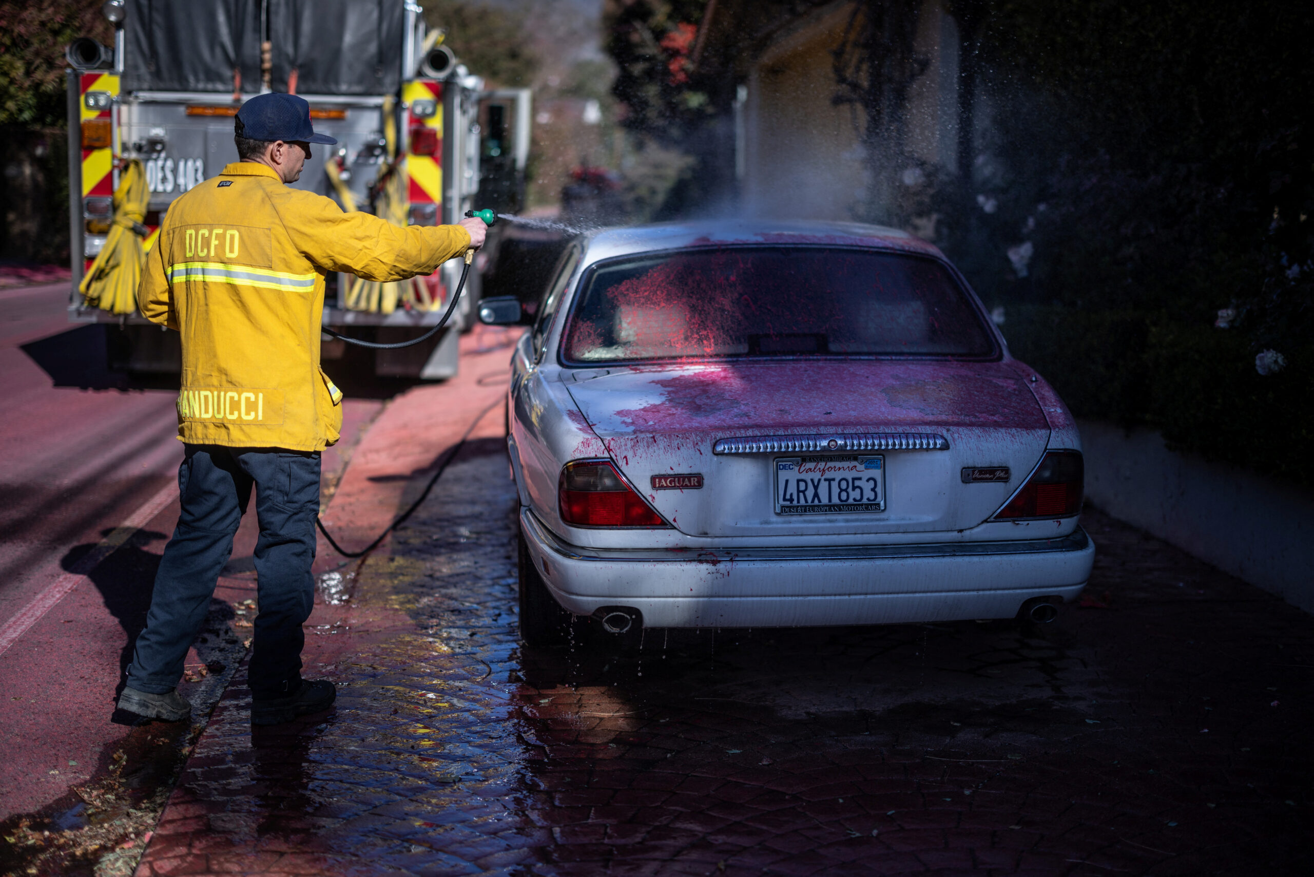 A firefighter cleans a car covered with fire retardant after the Palisades Fire at the Mandeville Canyon, a neighborhood of Los Angeles, California, U.S., January 13, 2025. REUTERS