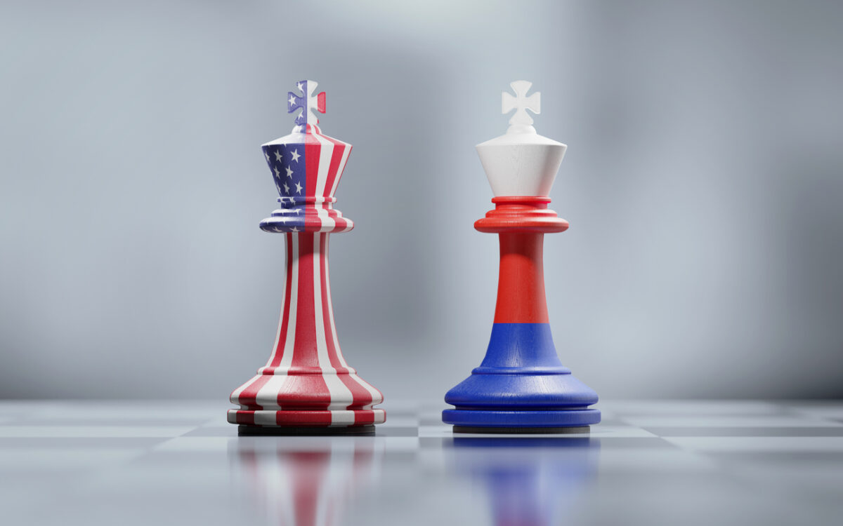 Two king chess pieces textured with American and Russian flags on black and white chessboard. Politics and checkmate concept. Horizontal composition with selective focus and copy space.