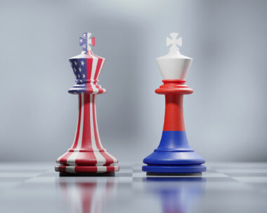 Two king chess pieces textured with American and Russian flags on black and white chessboard. Politics and checkmate concept. Horizontal composition with selective focus and copy space.