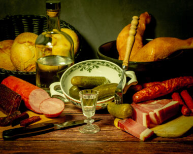 A stylized antique still life with meat, sausages, salami, lard and a glass of vodka
