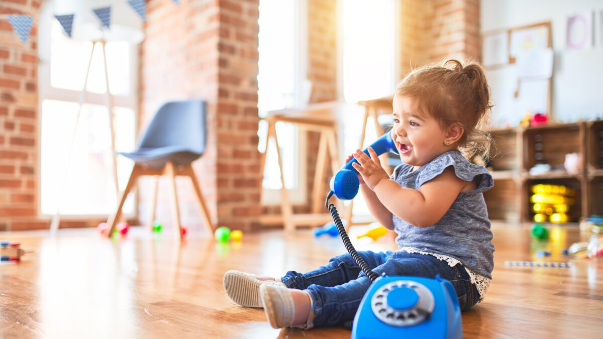 Beautiful toddler sitting on the floor playing with vintage phone at kindergarten