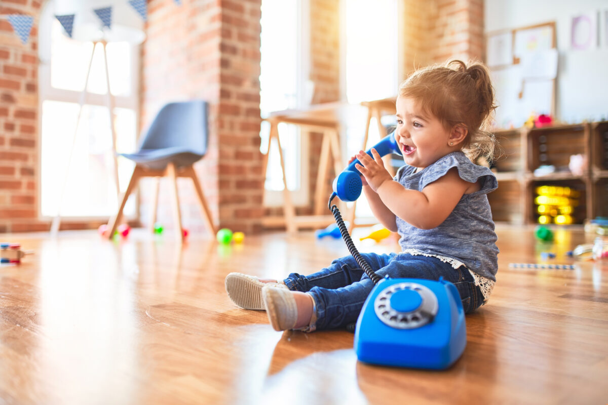 Beautiful toddler sitting on the floor playing with vintage phone at kindergarten