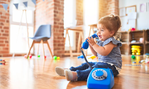 Beautiful toddler sitting on the floor playing with vintage phone at kindergarten
