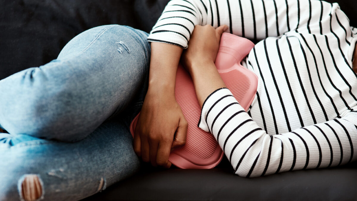 Cropped shot of a woman holding a hot water bottle against her stomach on the sofa at home