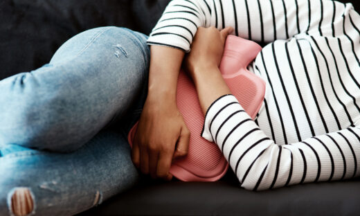 Cropped shot of a woman holding a hot water bottle against her stomach on the sofa at home
