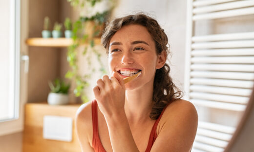 Smiling young woman brushing teeth in bathroom. Portrait of happy girl looking in mirror while using ecological toothbrush with whitening toothpaste. Beauty girl in bathroom cleaning teeth in the morning time.