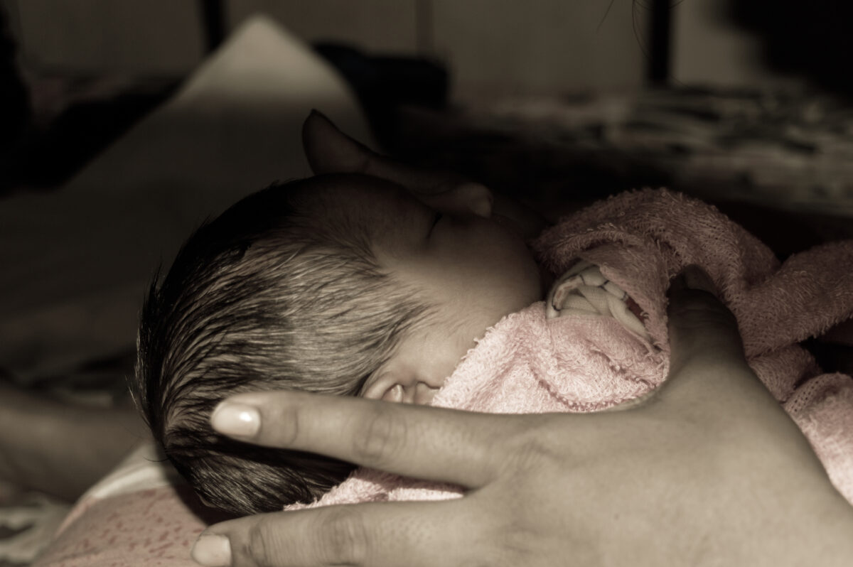 Beautiful Newborn baby boy (6 days old) laying in mother lap in prenatal hospital. Kid wrapped in warm clothing smiling and looking at his mother.
