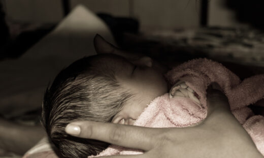 Beautiful Newborn baby boy (6 days old) laying in mother lap in prenatal hospital. Kid wrapped in warm clothing smiling and looking at his mother.