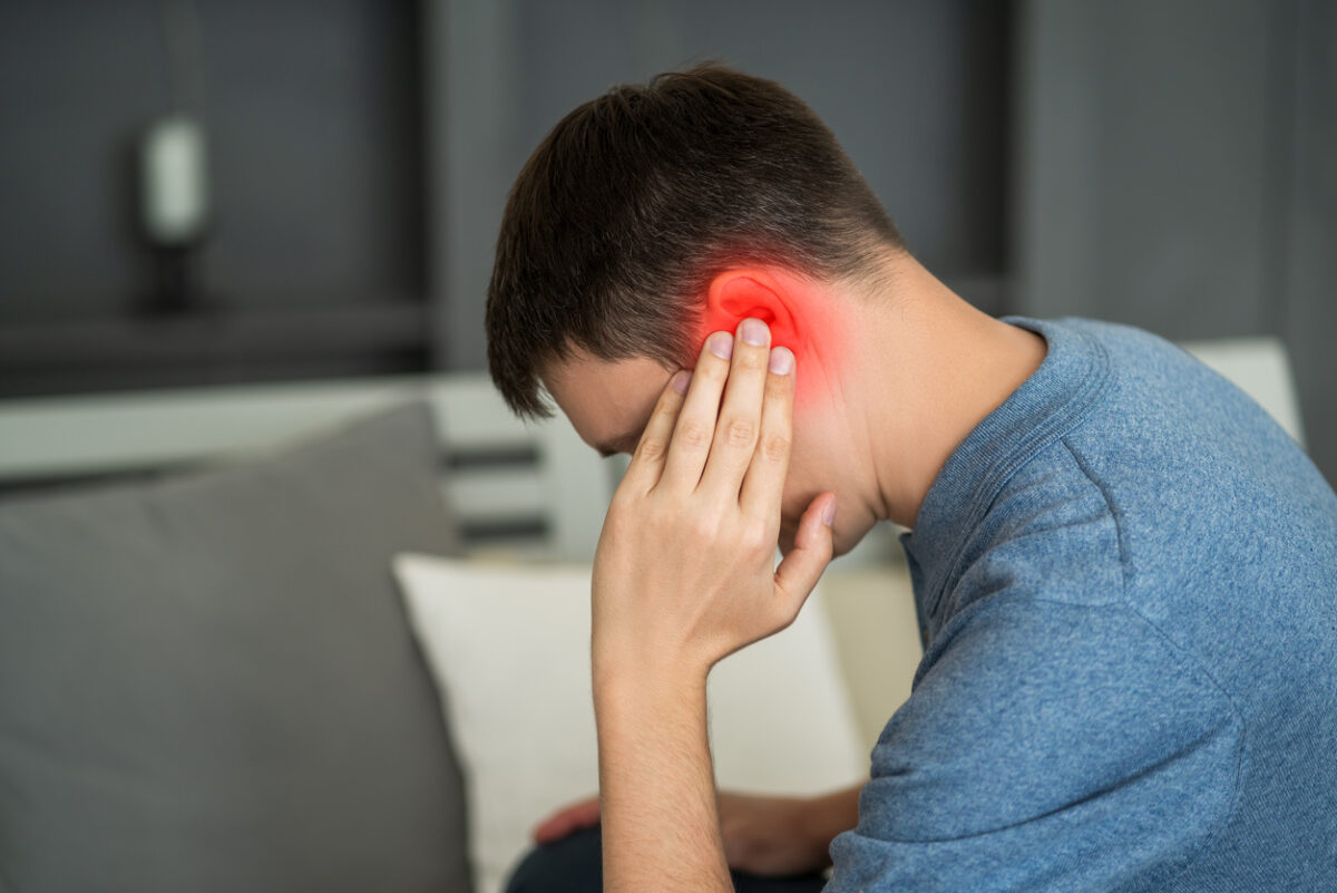 Man with earache, ear pain at home, painful area highlighted in red