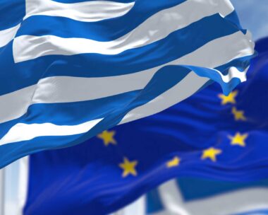 national flag of Greece waving in the wind with blurred european union flag in the background on a clear day