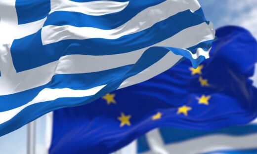 national flag of Greece waving in the wind with blurred european union flag in the background on a clear day