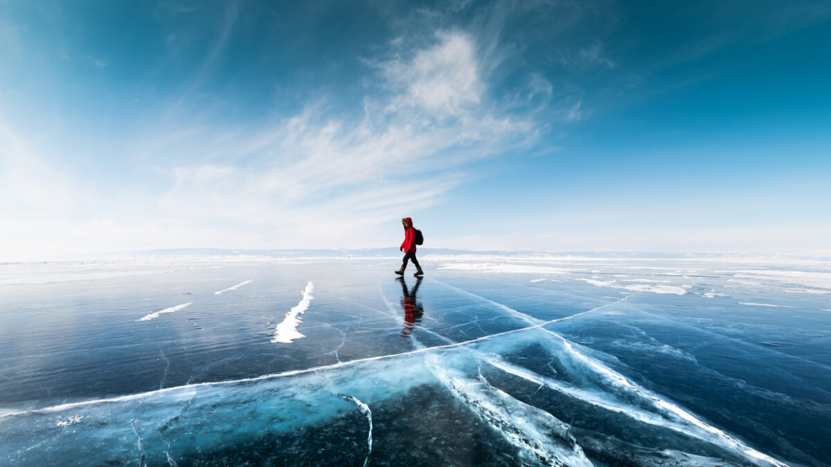 Man tourist walking on the ice of Baikal lake. Winter landscape of Baikal lake, Siberia, Russia. Blue transparent cracked ice and the blue sky.
