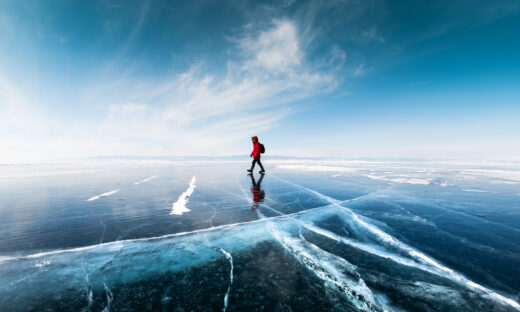 Man tourist walking on the ice of Baikal lake. Winter landscape of Baikal lake, Siberia, Russia. Blue transparent cracked ice and the blue sky.