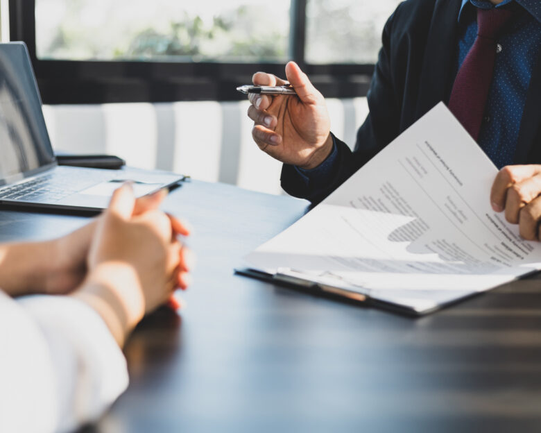 Businessman in suit in his office showing an insurance policy and pointing with a pen where the policyholder must to sign. Insurance agent presentation and consulting insurance detail to customer