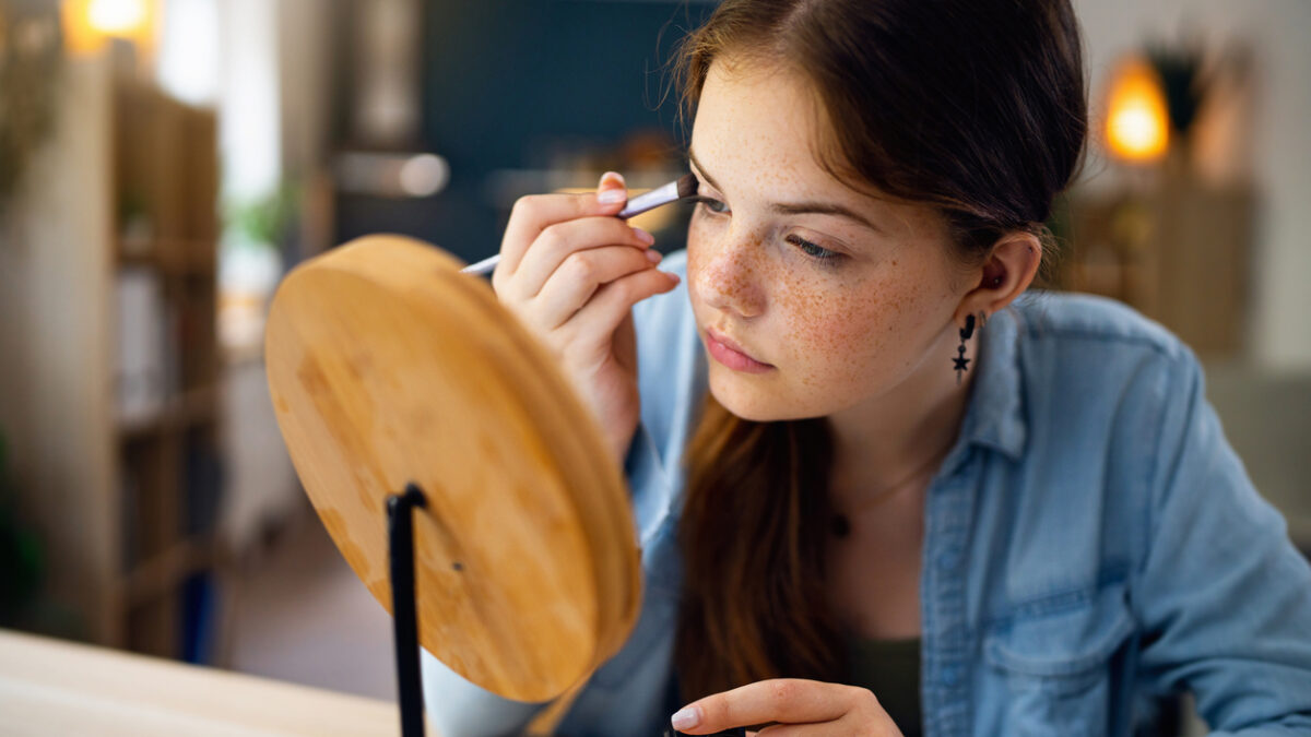 Teenage girl doing make-up in front of the mirror at her home