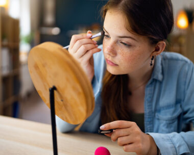 Teenage girl doing make-up in front of the mirror at her home