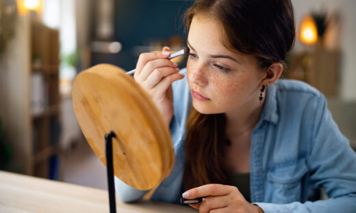 Teenage girl doing make-up in front of the mirror at her home
