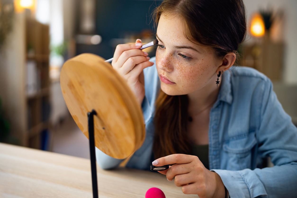 Teenage girl doing make-up in front of the mirror at her home