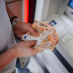 A person holding euro banknotes infront of an atm