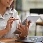 Close up image of a woman using a tablet infront of a laptop