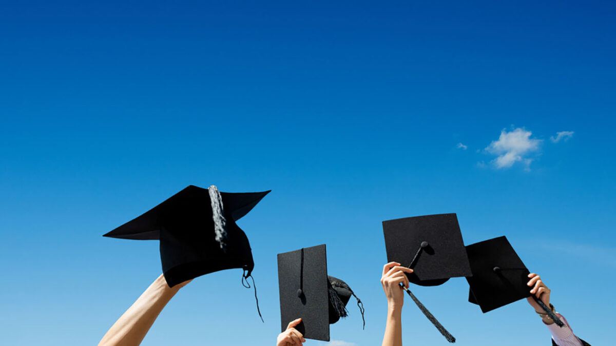 Four hands holding graduation hats against blue sky