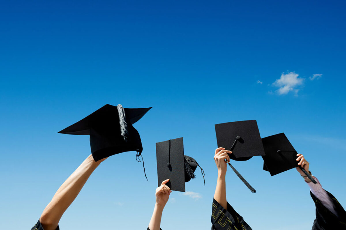Four hands holding graduation hats against blue sky