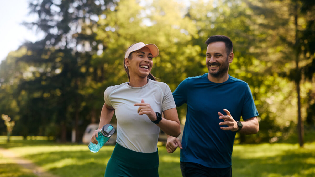 Happy athletic couple having fun while running together in nature. Copy space.