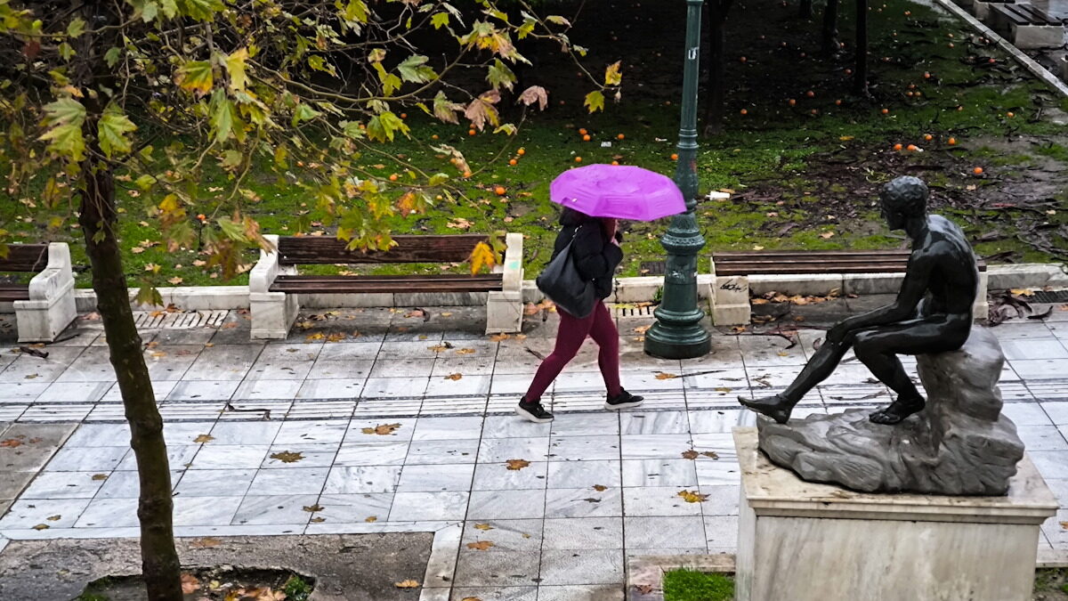 Μία γυναίκα περπατάει στη βροχή κρατώντας μία ομπρέλα