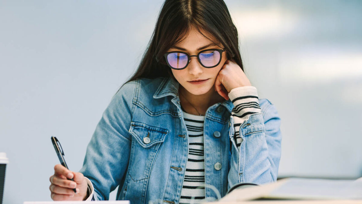 Woman student sitting at college library and studying. Girl reading notes at college campus.