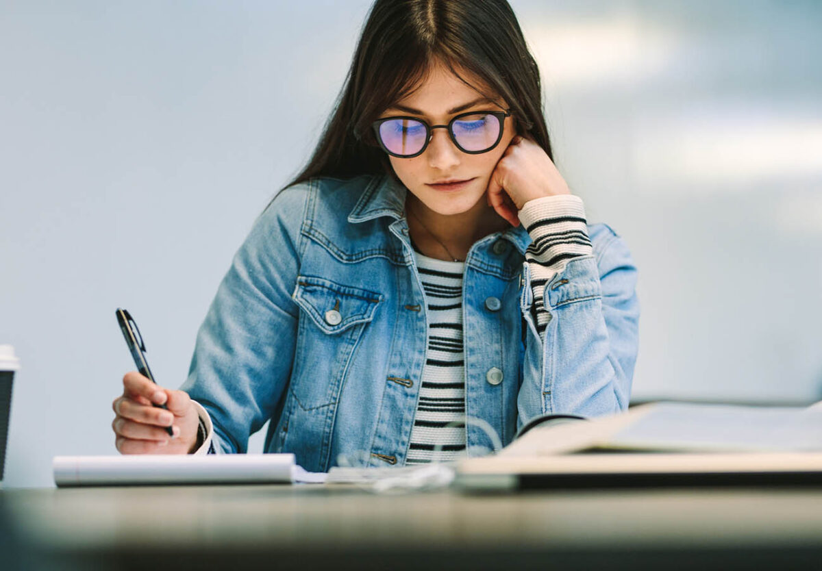 Woman student sitting at college library and studying. Girl reading notes at college campus.