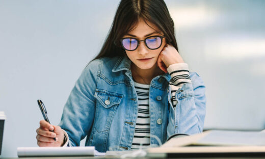 Woman student sitting at college library and studying. Girl reading notes at college campus.