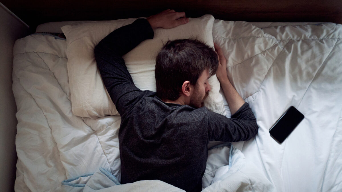 Young male sleeping in the bed only himself during the day smartphone next to him