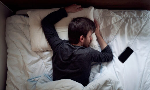 Young male sleeping in the bed only himself during the day smartphone next to him