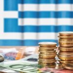 Euro banknotes and coins in front of the national flag of Greece