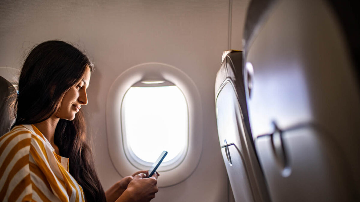 Young smiling Latin woman using mobile phone in the airplane.