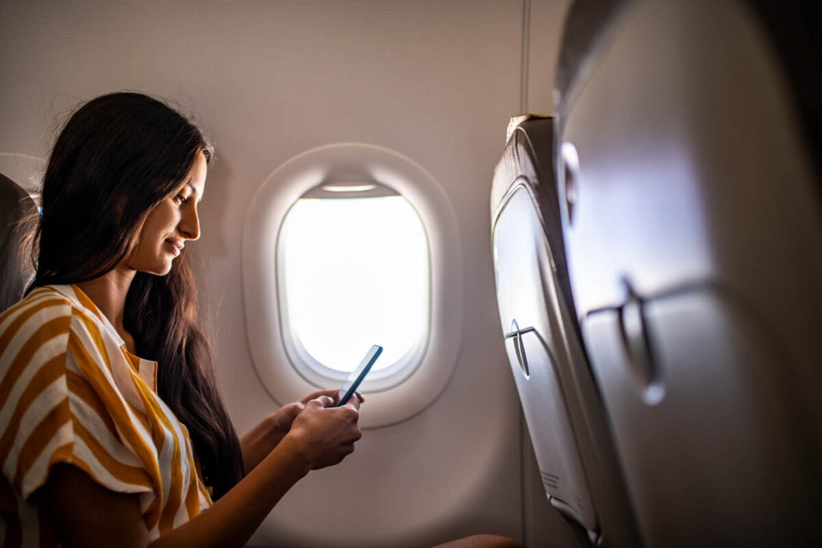 Young smiling Latin woman using mobile phone in the airplane.