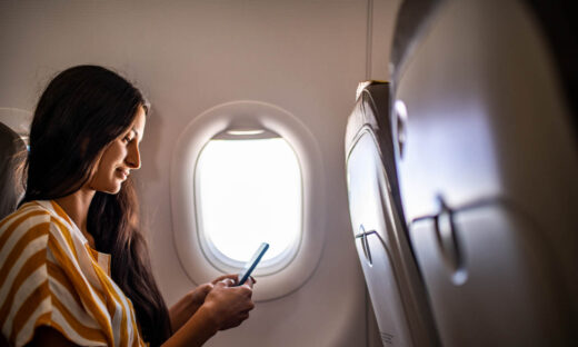 Young smiling Latin woman using mobile phone in the airplane.