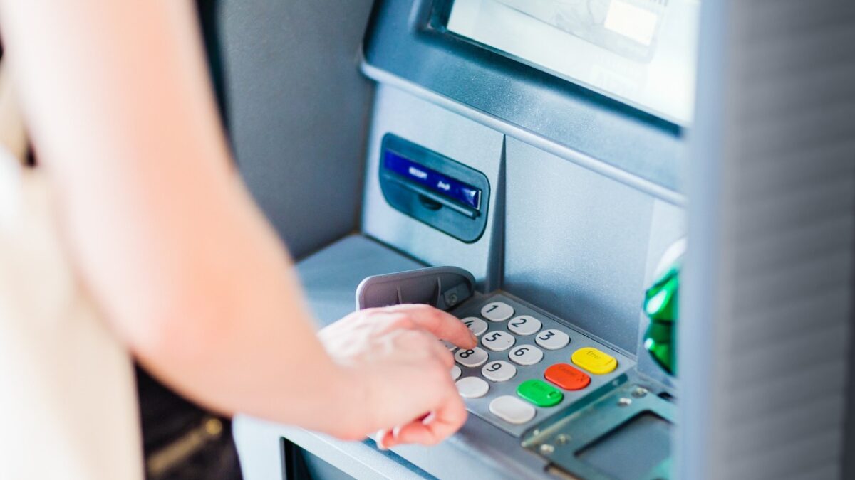 An adult person pressing on ATM machine keypad number to withdraw cash money