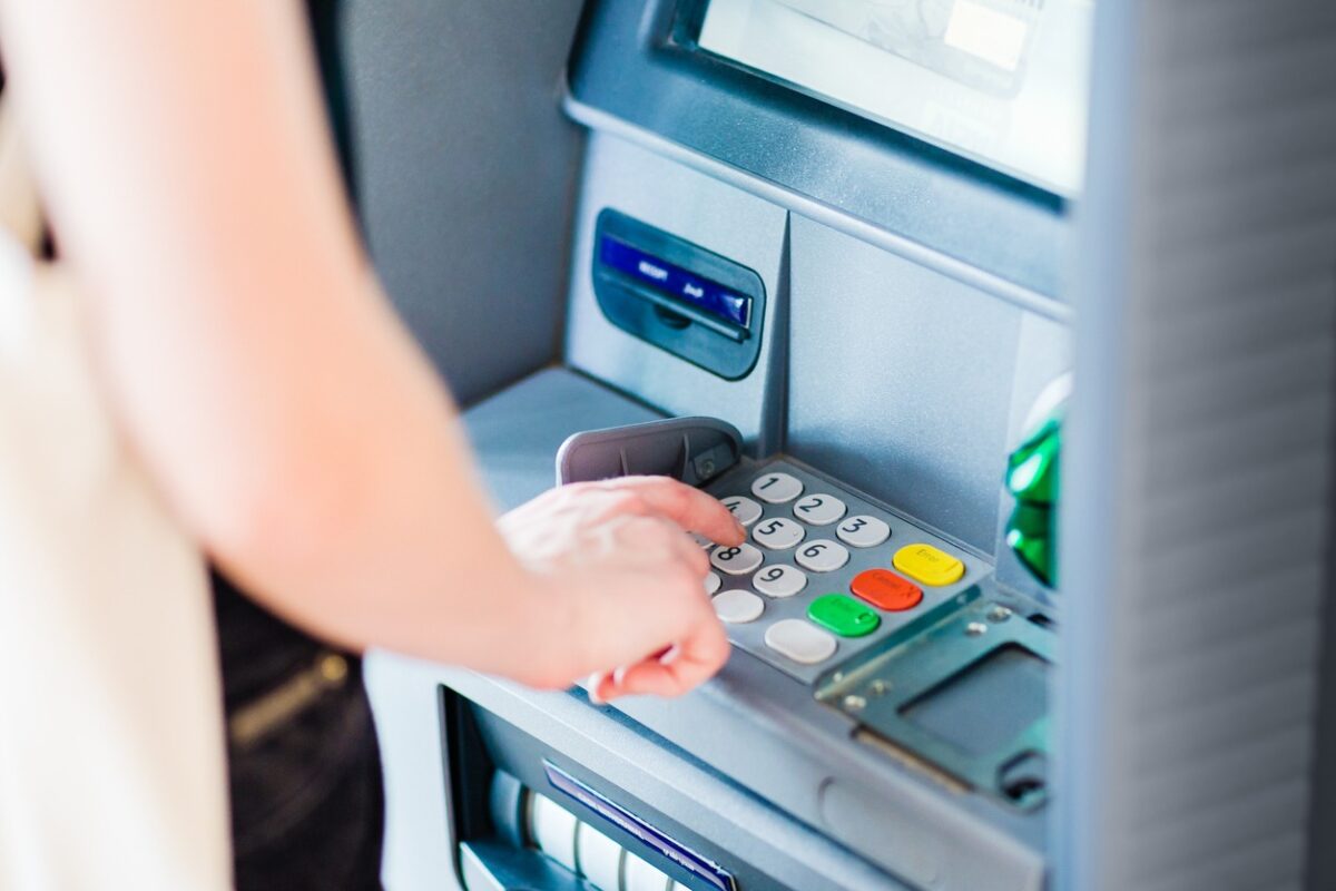 An adult person pressing on ATM machine keypad number to withdraw cash money