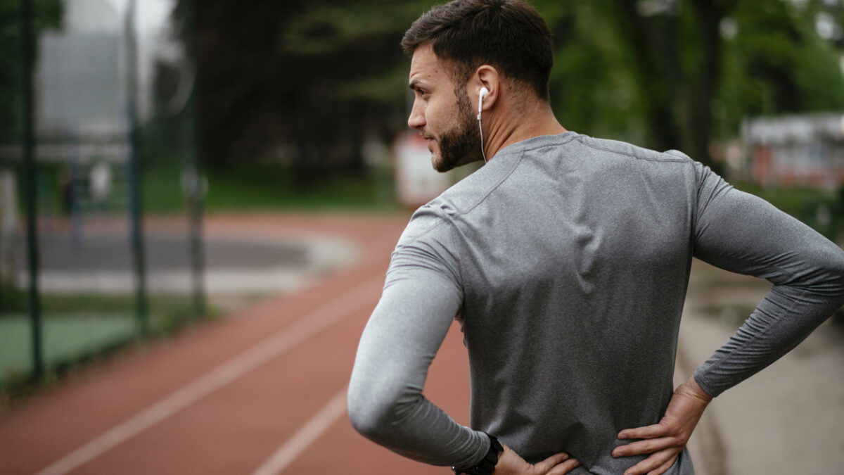 Sportsman suffering from backache at park outdoors. Back Pain. Sport injury